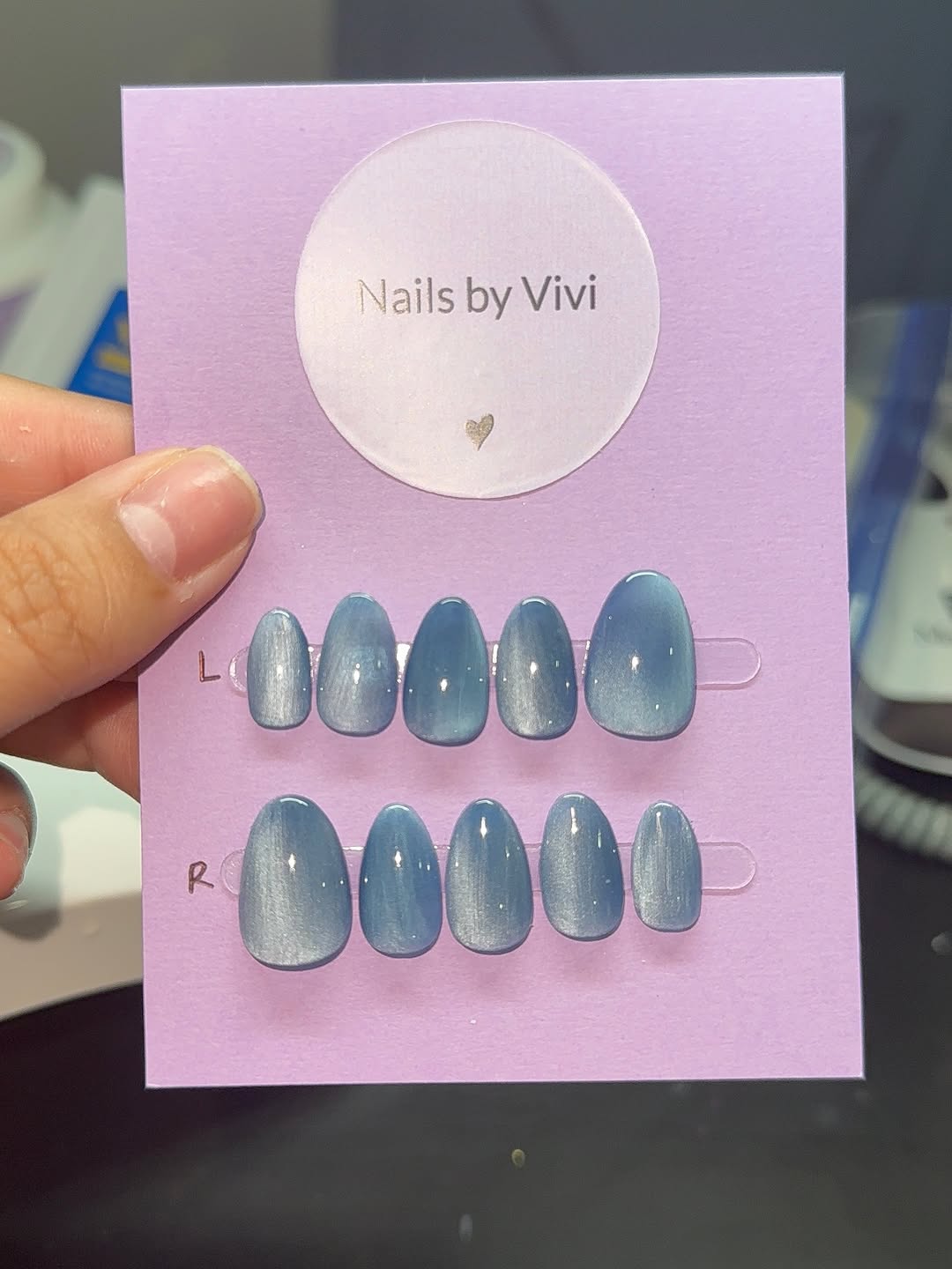 Blue cat-eye press-on set on a lilac Nails by Vivi card.