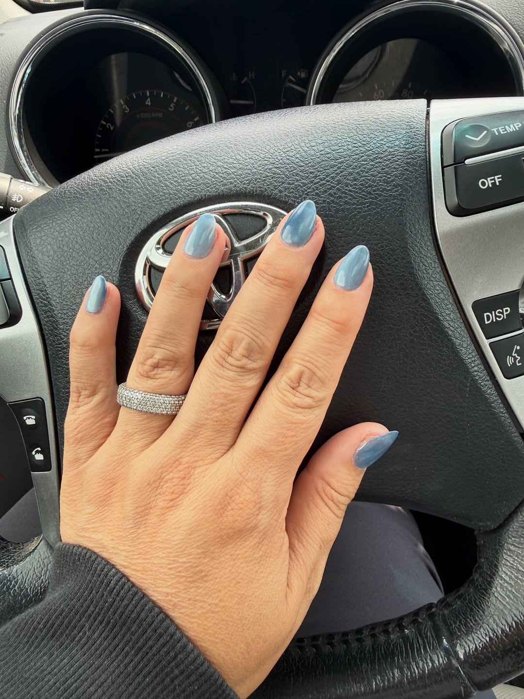 Short almond blue cat-eye press-ons worn on a hand resting on a steering wheel.