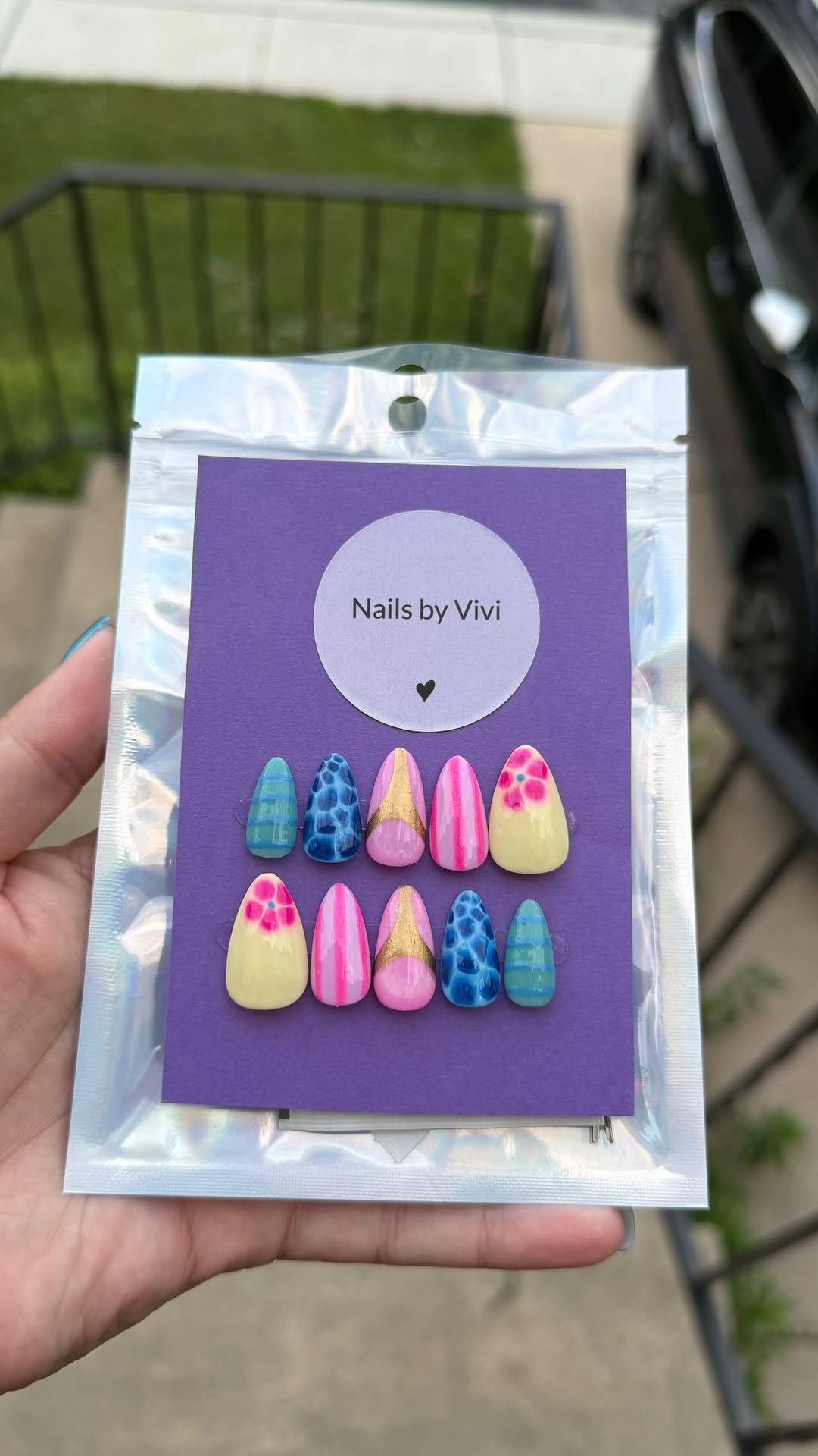 Colorful mixed press-on set on a purple Nails by Vivi card inside a holographic bag.